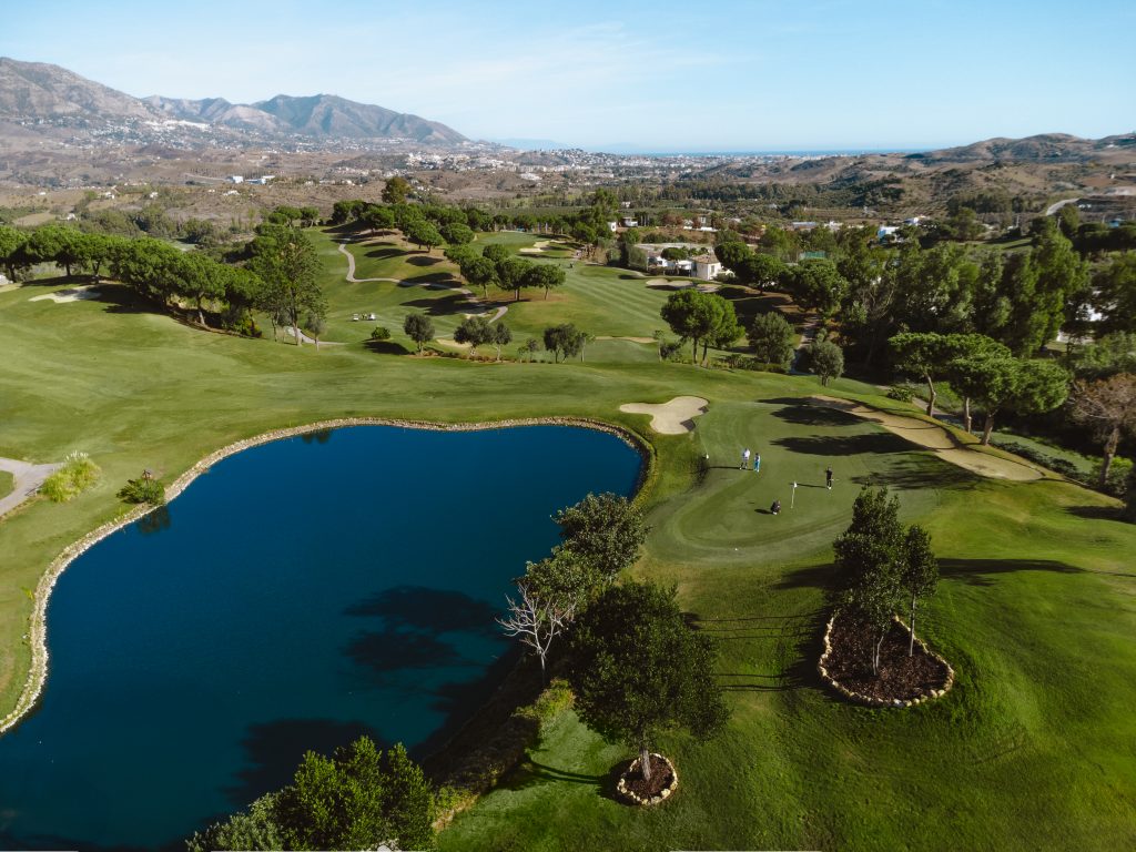 Golfanlage La Cala Golf Club mit einzelnen Golfplätzen und See, im Hintergrund Stadt, Gebirge und Meer