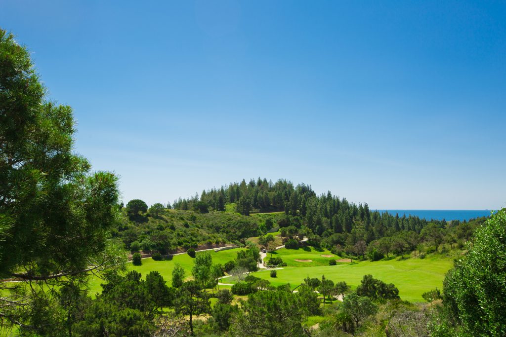 Blick auf Loch 12 und 13 im Golfclub El Chaparral, kleiner Wald und Meer im Hintergrund