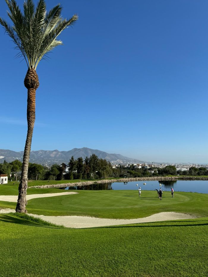Blick auf Golfplatz mit See im Cerrado del Águila Golf & Resort, Gebirge und Stadt im Hintegrund