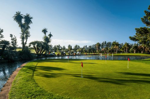 Golfplatz mit roten Fahnen im Golf Club Santa Clara Marbella, See und Palmen im Hintergrund