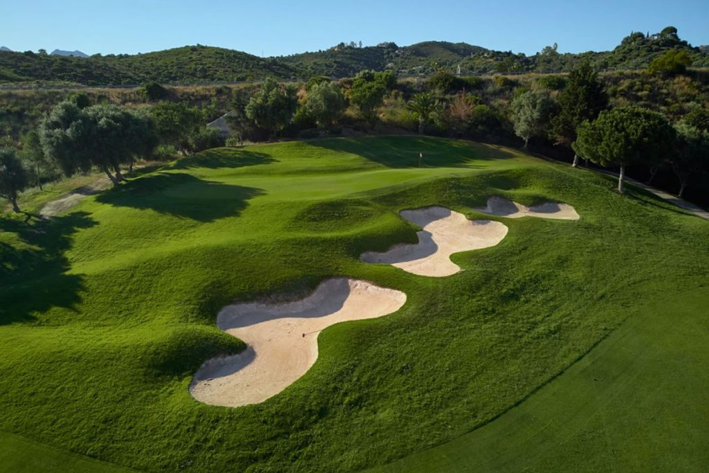 Blick von oben auf einen Golfplatz des Marbella Golf & Country Clubs mit 3 Bunkern, hügelige Landschaft im Hintergrund