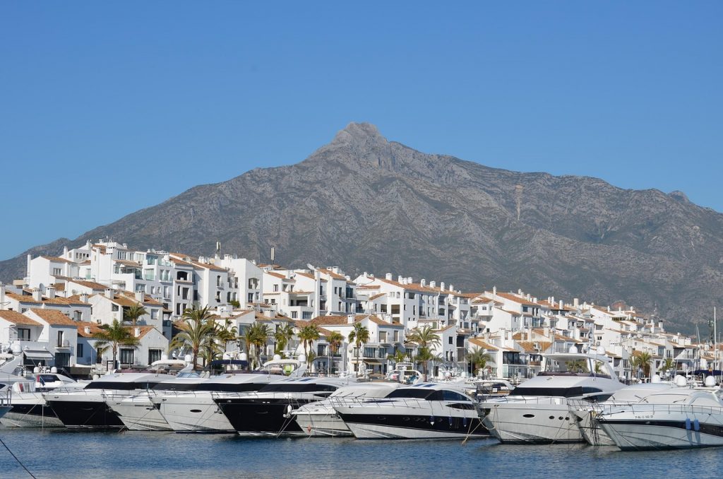 Blick auf die Promenade von Marbella mit Booten und weißen Häusern, Berg im Hintergrund